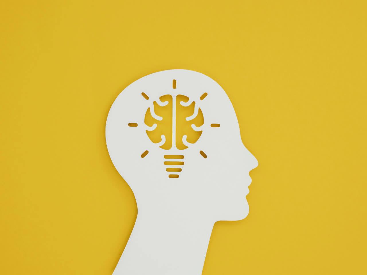 A paper cut-out of a head with a lightbulb, on a yellow background